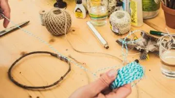 Hände basteln mit Schnur auf Holztisch.