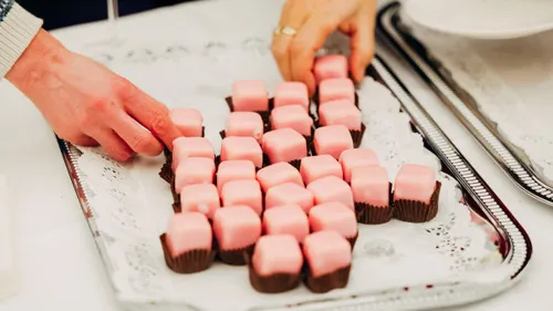 Hands arranging pink pastries on a tray.
