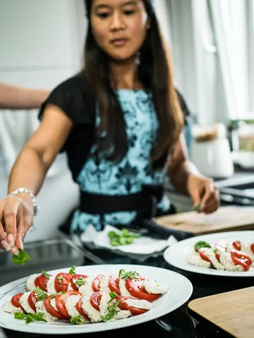 Eine Frau garniert einen Teller mit Tomaten und Kräutern.