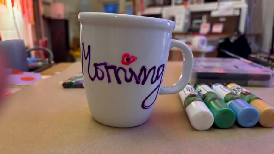 Tasse mit 'morning' Text auf unordentlichem Schreibtisch.