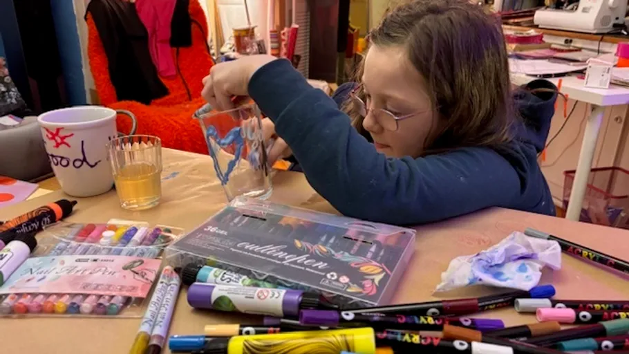 Child painting on glass amidst art supplies.