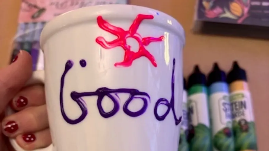 Hand holding a decorated mug with markers.