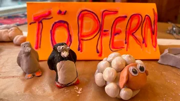 Tonfiguren mit 'Töpfern'-Schild im Hintergrund.