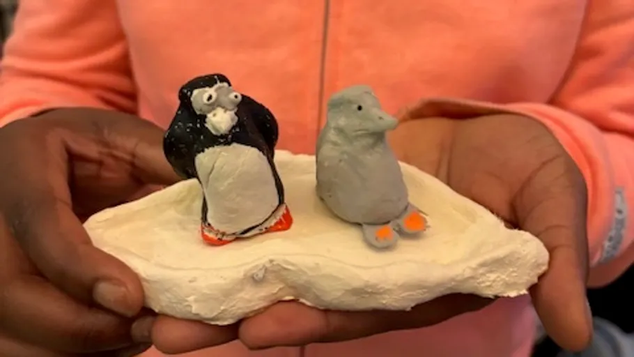 Hands holding clay penguins on white base.