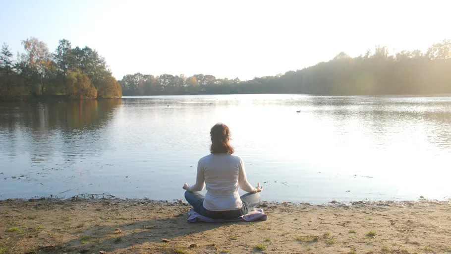 Person meditating by a serene lakeside.