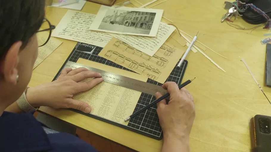 Person measuring paper with ruler and pencil.