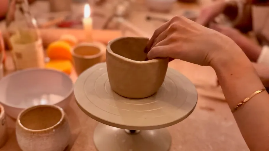 Hand shaping clay bowl on pottery wheel.