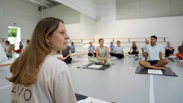 Personen auf Yogamatten im Studio sitzend.