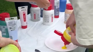 People pouring paint onto paper plate outdoors.