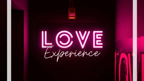 Neon sign saying 'Love Experience' in dark room.