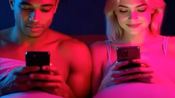 Two people using phones in bed, colorful lighting.