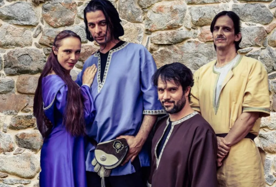 Four people in historical costumes, stone wall backdrop.