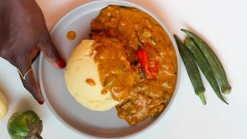 Teller mit Fufu und Soße, Hand berührt Teller.