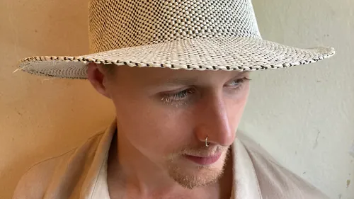 Person wearing woven hat against plain wall.