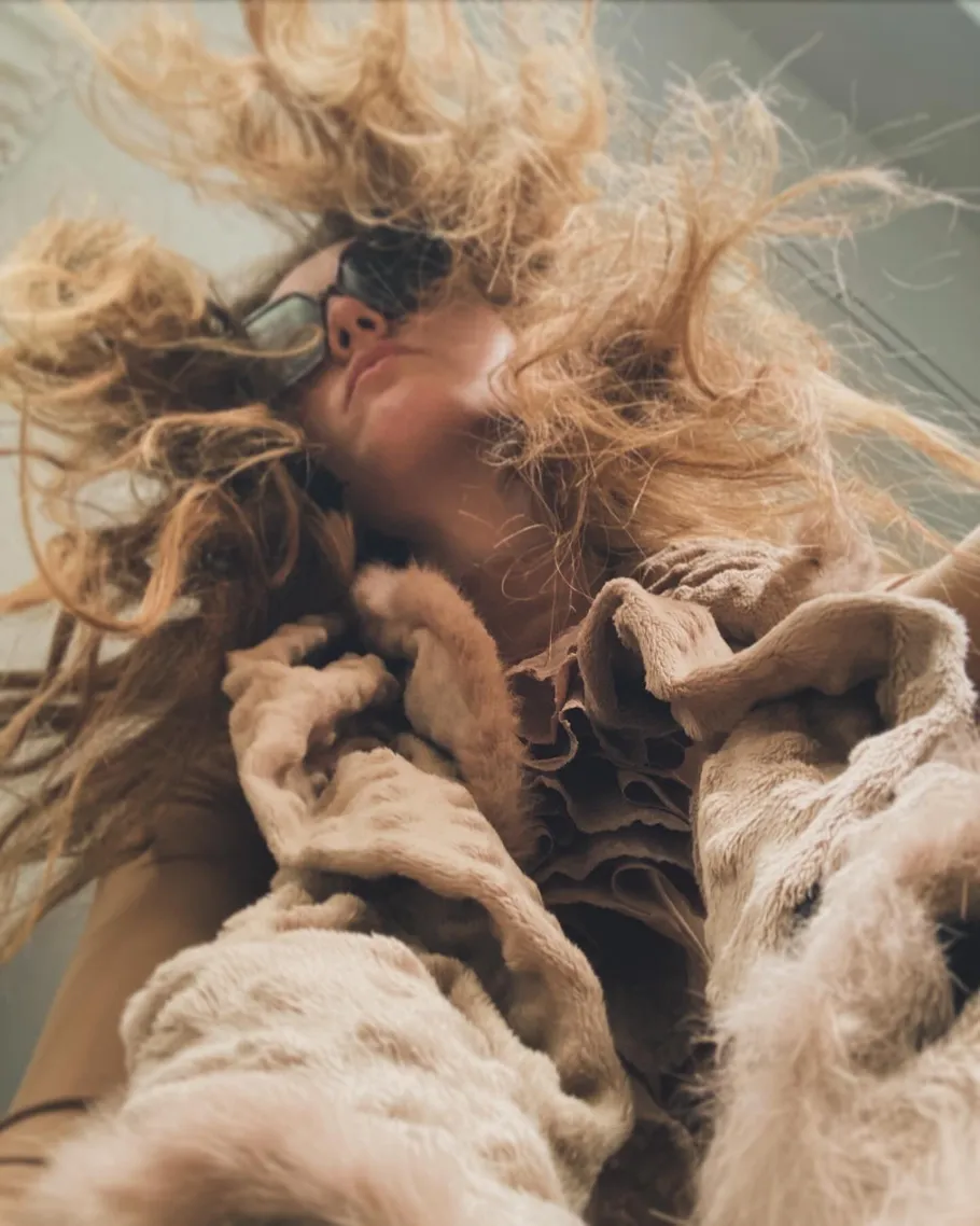 Person wearing fur coat, sunglasses indoors.