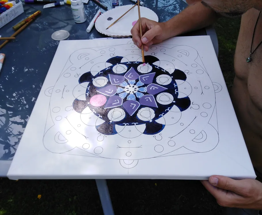 Person painting a mandala design outdoors on canvas.