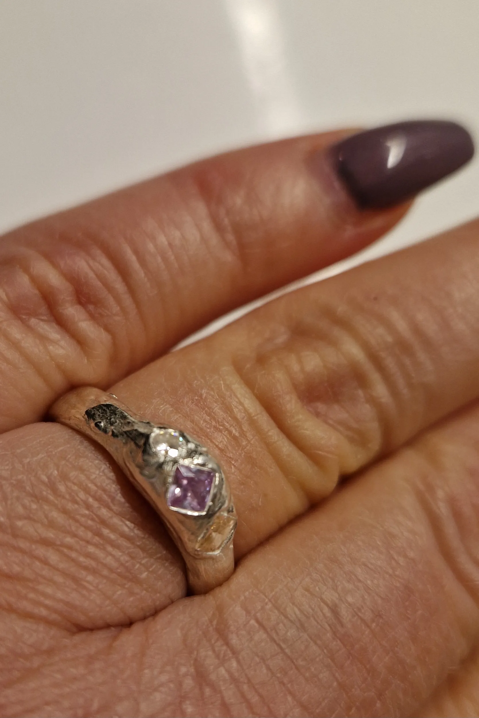 Hand trägt silbernen Ring mit lila Stein.