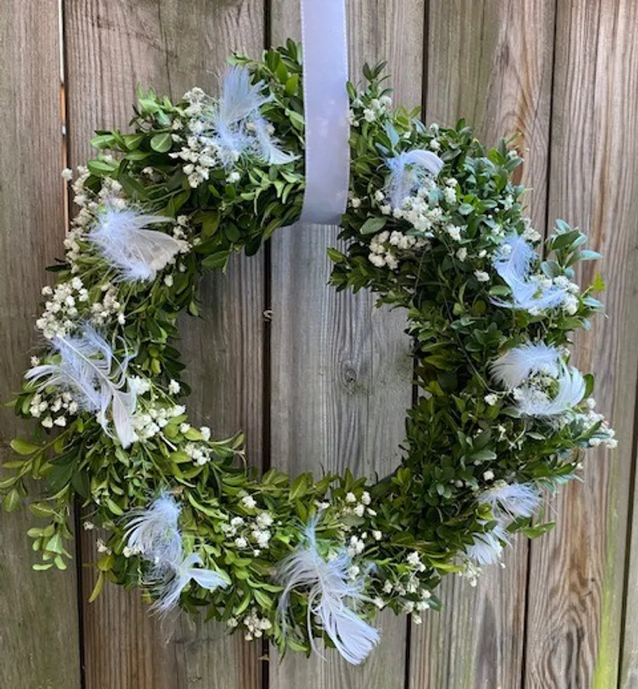 Green wreath with white flowers on fence.