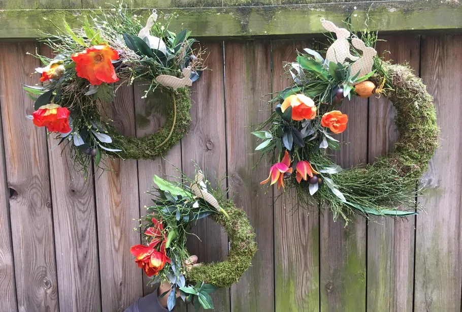 Drei Blumenkränze an Holzzaun.