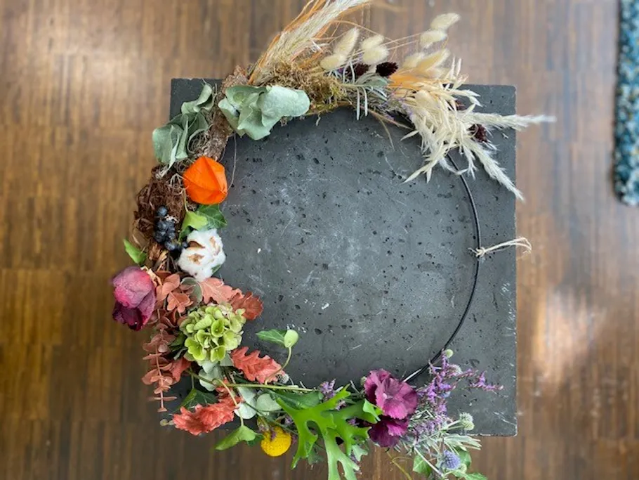 Blumenkranz auf Betonblock, Holzfußboden.