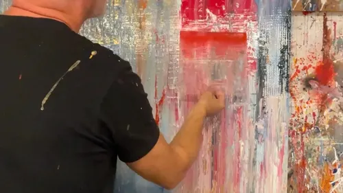 Man painting abstract art on large canvas.