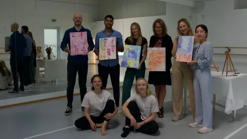 Group of people holding paintings in studio.