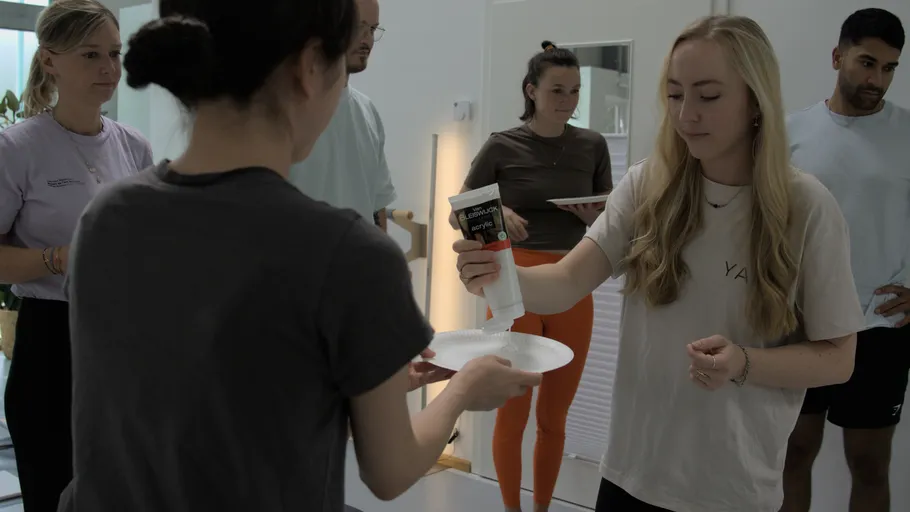 Woman squeezing paint onto plate, surrounded by people.