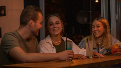 Three friends smiling while drinking at bar.