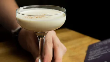 Person holding creamy cocktail at table.