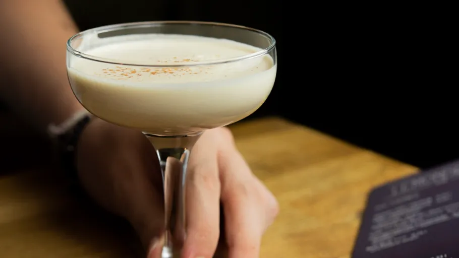 Person holding creamy cocktail at table.