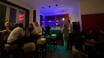 Schummrig beleuchtete Bar mit Leuten beim Reden.