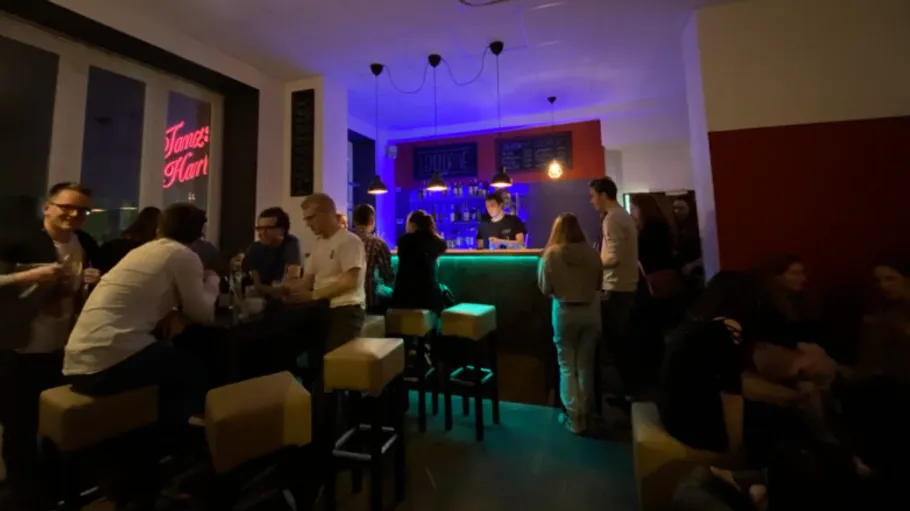 Schummrig beleuchtete Bar mit Leuten beim Reden.