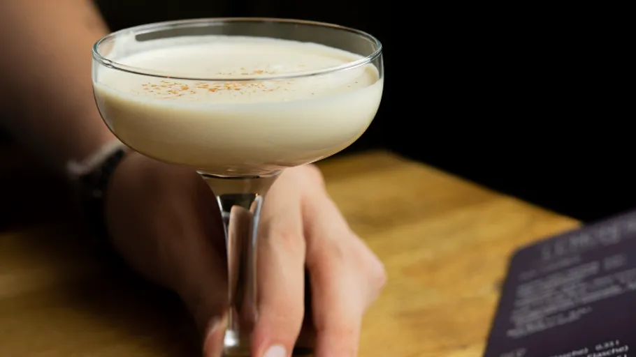 Hand holding creamy cocktail in dimly lit bar.