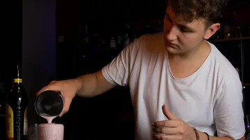 Bartender pouring drink into glass at bar.