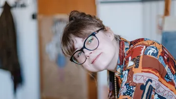 Frau lächelt, trägt Brille, drinnen.
