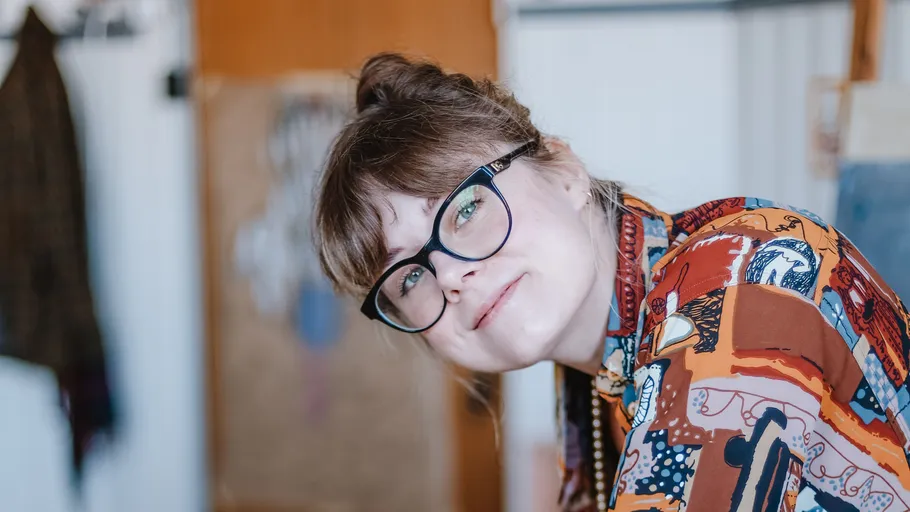 Frau lächelt, trägt Brille, drinnen.