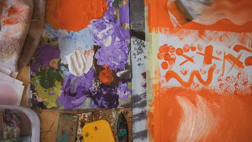 Paint palette beside an orange-painted canvas.