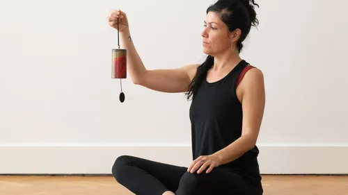 Woman holding chime, sitting cross-legged indoors.