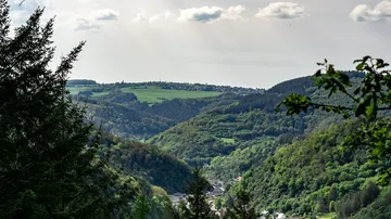 Green hills and village under cloudy sky.