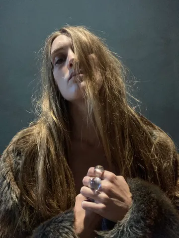 Person with long hair and fur coat indoors.
