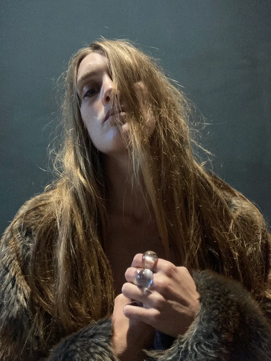 Person mit langem Haar und Pelzmantel drinnen.