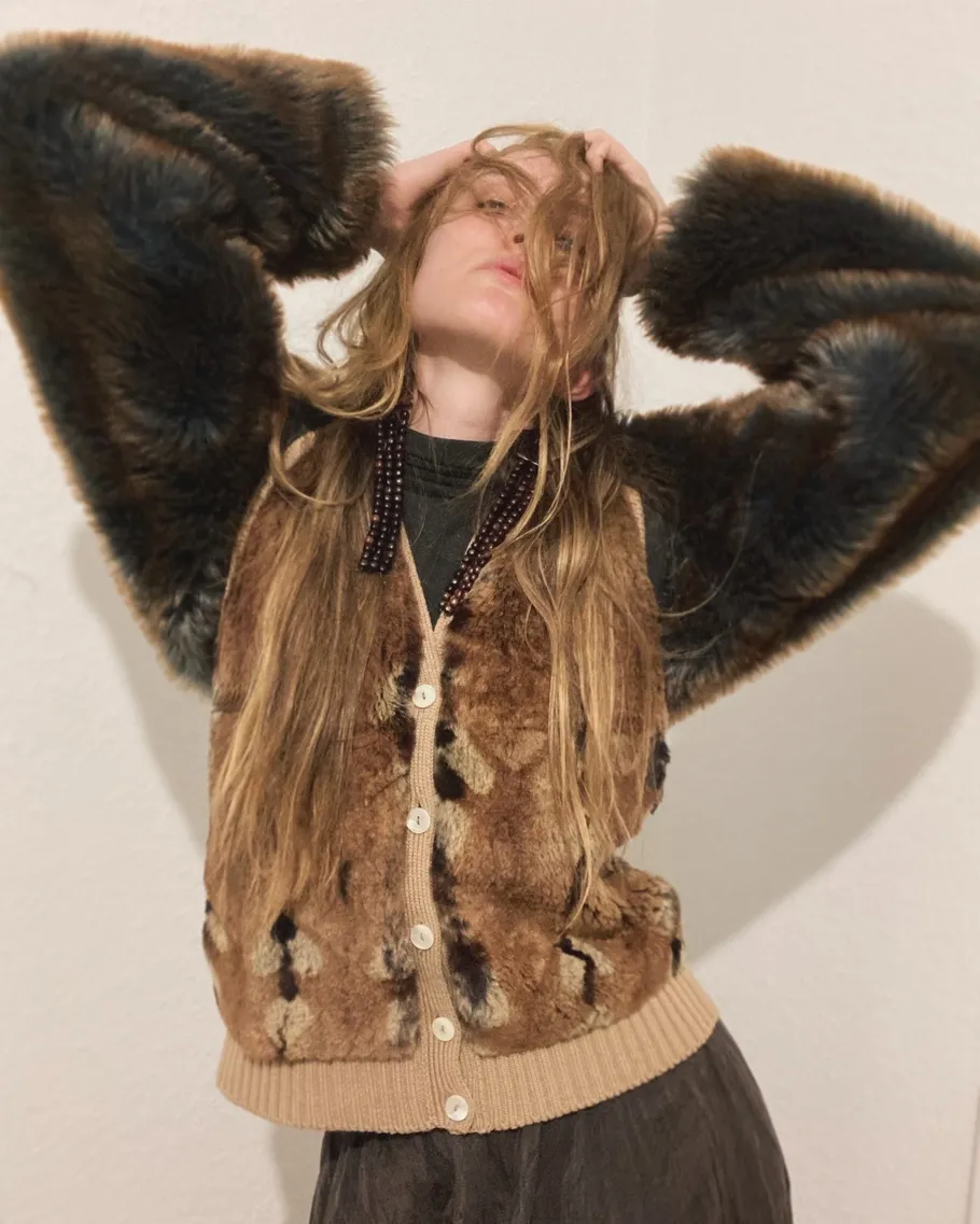 Person posing in fur coat, hands in hair.