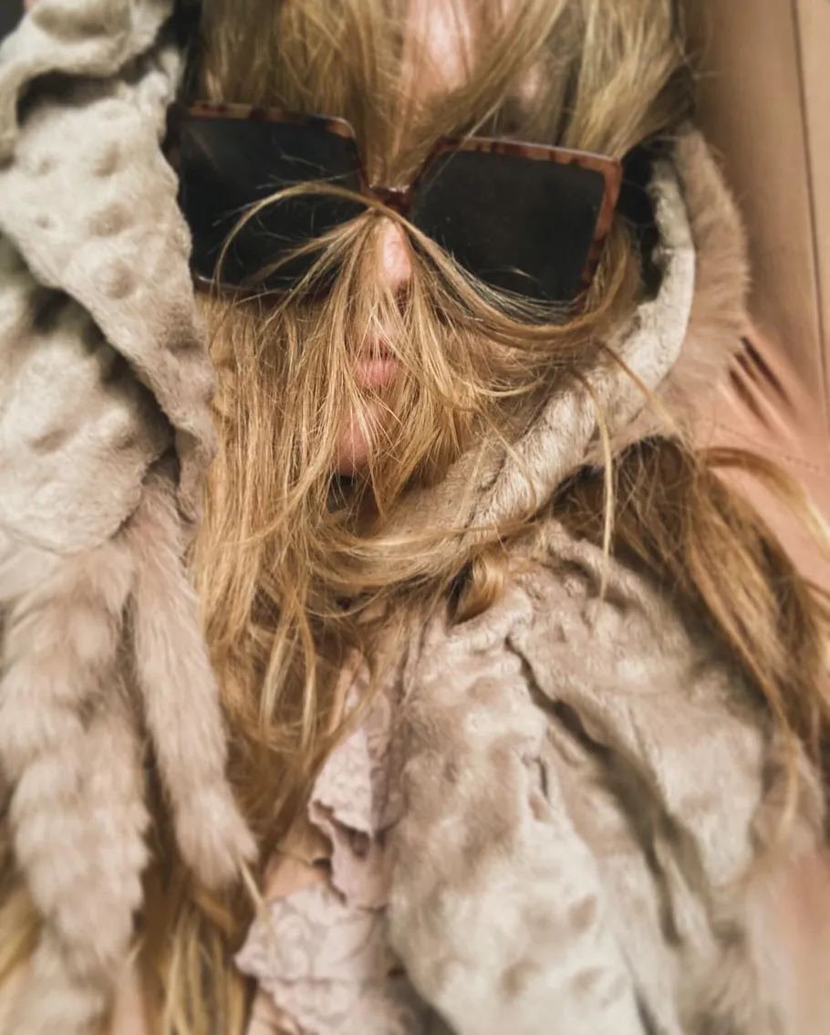 Person mit Sonnenbrille und Haar im Gesicht.