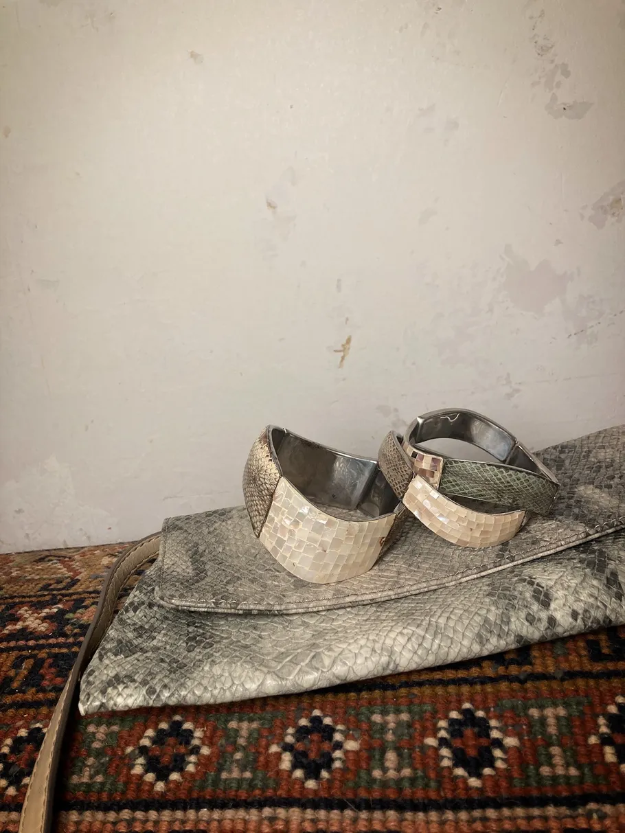 Bracelets on snakeskin purse on patterned rug.
