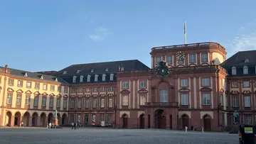 Large baroque palace with courtyard, people walking.