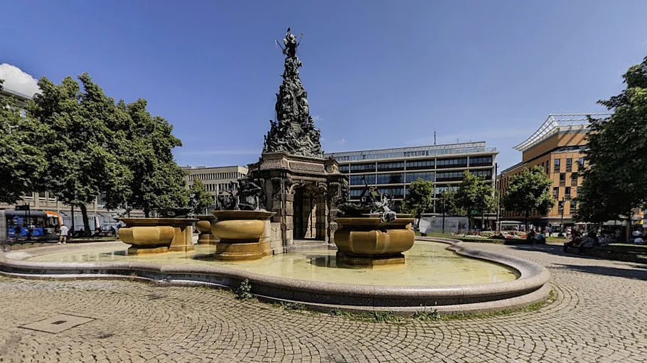 Statue fountain surrounded by buildings and trees.