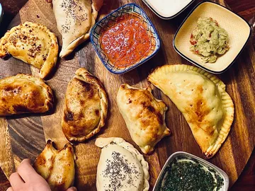 Teigtaschen liegen auf einem Holzbrett mit Dips.