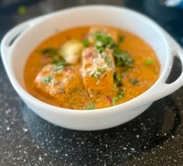 Weiße Schüssel mit Curry und Kräutern auf Tisch.