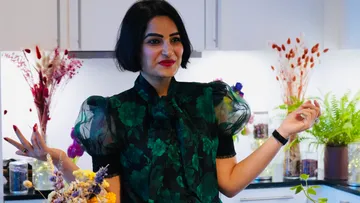 Woman smiling in kitchen, holding flowers.