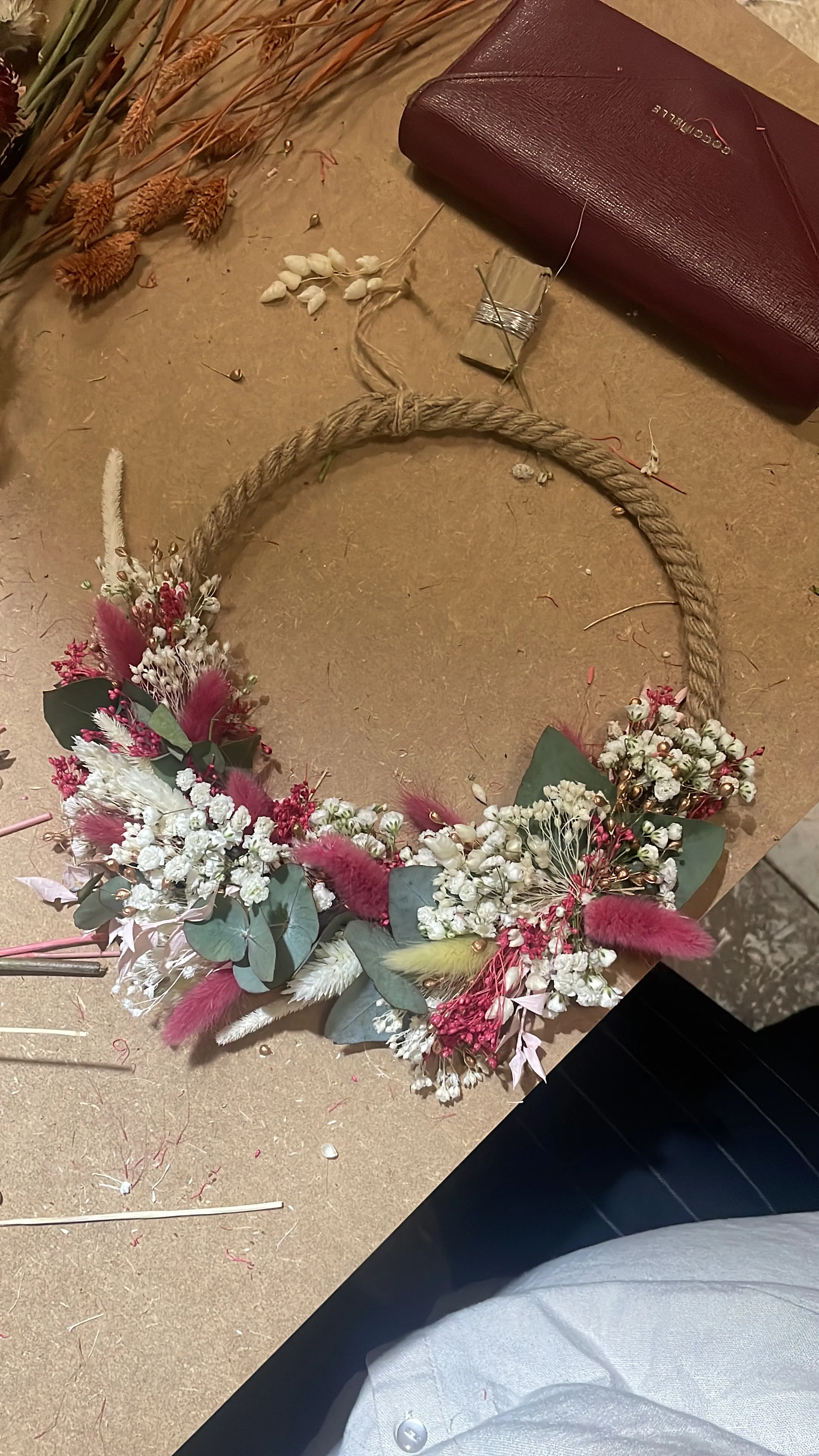 Floral wreath on table with crafting materials.